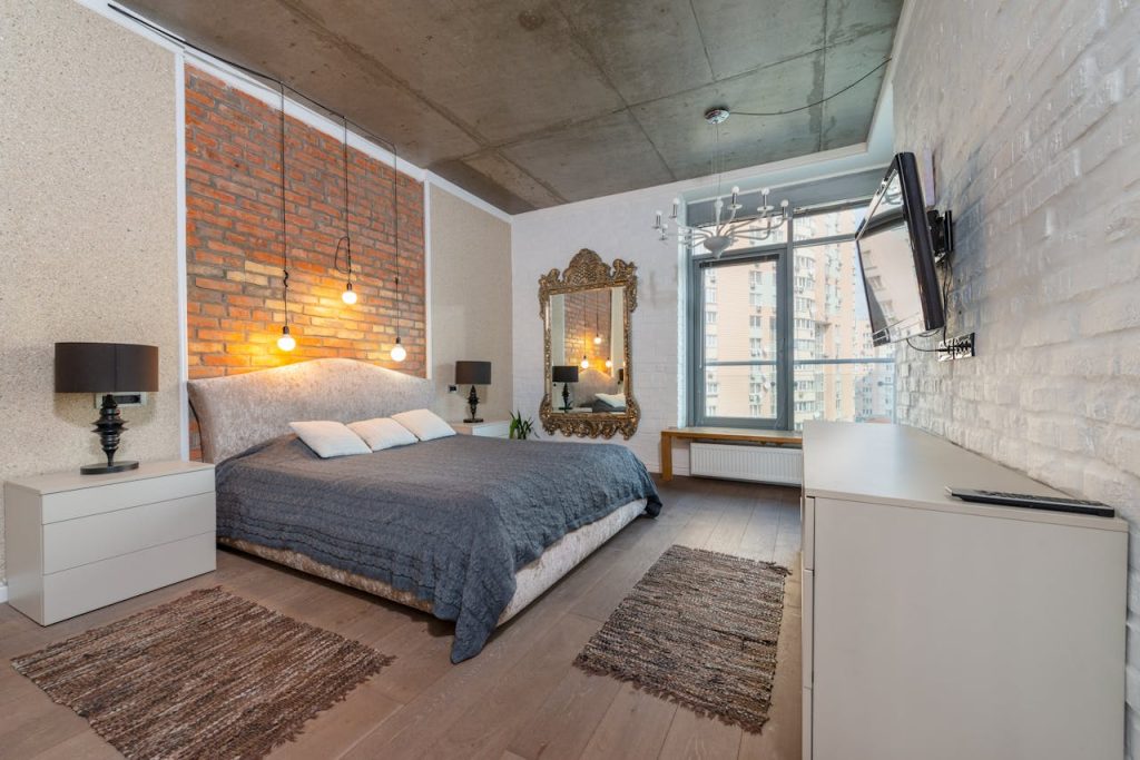 Spacious industrial-style bedroom with brick wall, cozy bed, and modern decor.